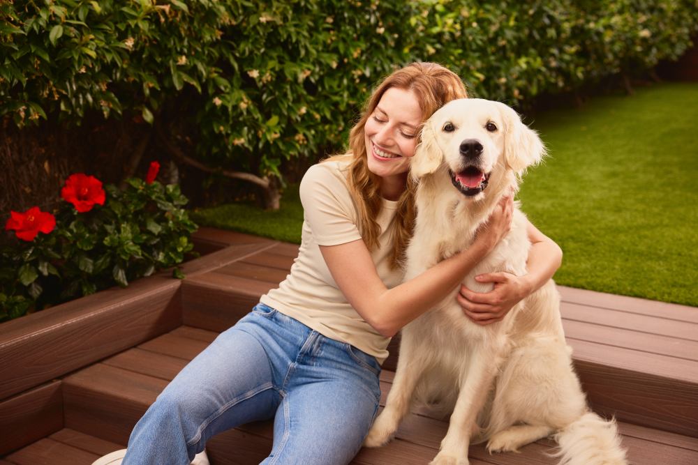 Una mujer sentada junto a un perro en una zona ajardinada, imagen oficial de CaixaBank para MyBox Mascotas